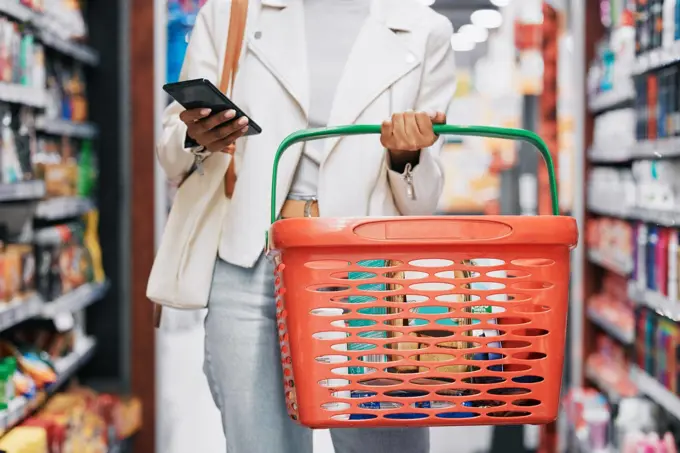 Grocery shopping, retail and black woman with phone in store, shop or supermarket. Girl buying groceries or purchasing products at a food mart or outlet while texting on mobile or smartphone.