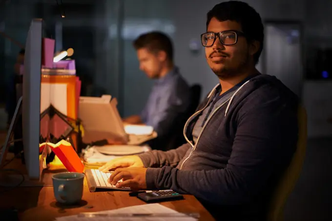 Getting the job done. a group of young coworkers working in a dimly-lit office.