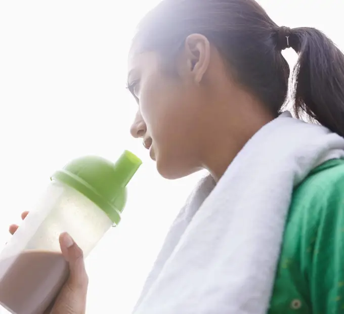 Staying healthy. A young ethnic woman drinking a sports drink outdoors.