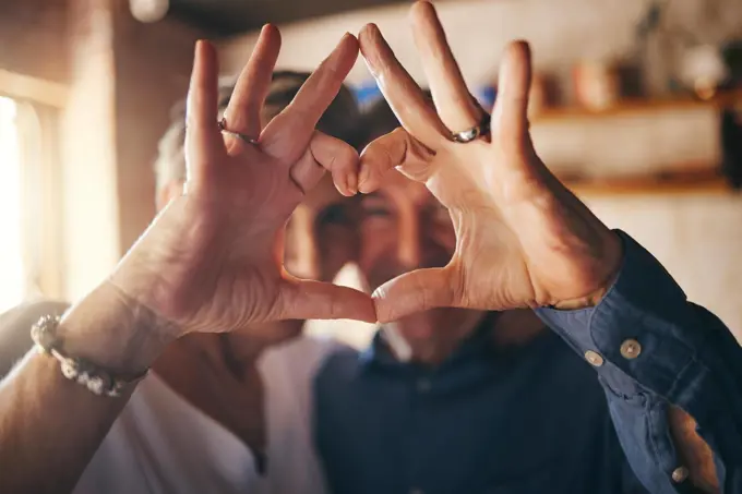 Love, hands and heart sign with senior couple relax and bonding in their home together, cheerful and in love. Support, soulmate and loving man and woman sharing romantic moment and enjoy relationship