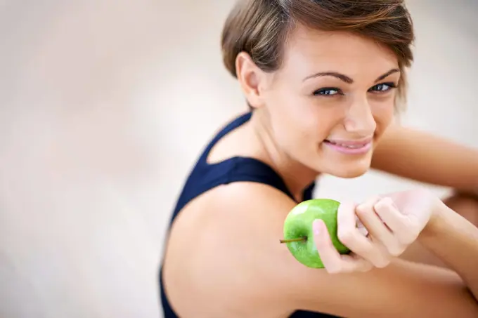 Building blocks for a happy healthy life. a sporty young woman sitting on a gym floor eating an apple.