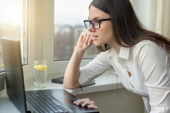 Young business woman with glasses working on laptop computer at home