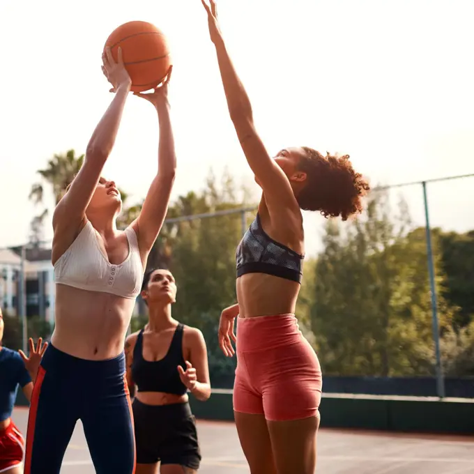 Trying my luck here. a diverse group of sportswomen playing a competitive game of basketball together during the day.