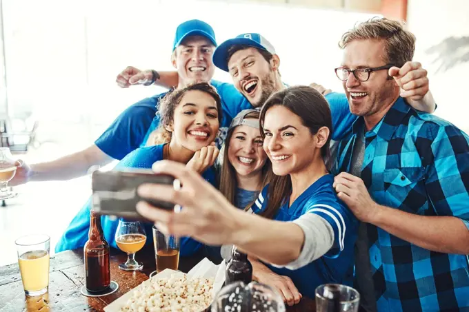 Kicking off the game with a selfie. a group of friends taking a selfie while watching a sports game at a bar.