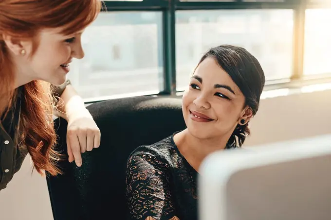 Thats why I love working with you. two young businesswomen using a computer together in a modern office.