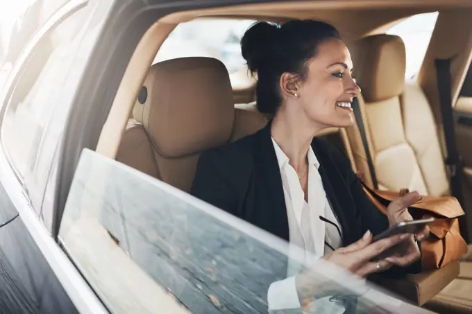 I am excited to get working. a cheerful young businesswoman seated in a car as a passenger while texting on her phone on her way to work.