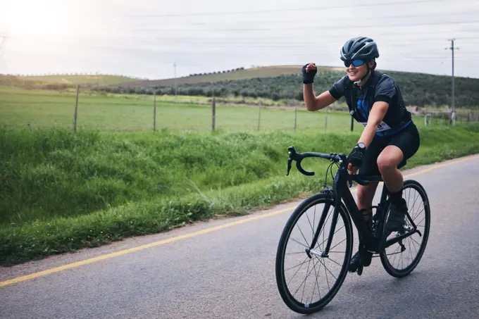 Fitness, win and woman in celebration while cycling in nature with energy for a race, marathon or competition. Sports, workout and female athlete cyclist cheering for cardio exercise on outdoor road.