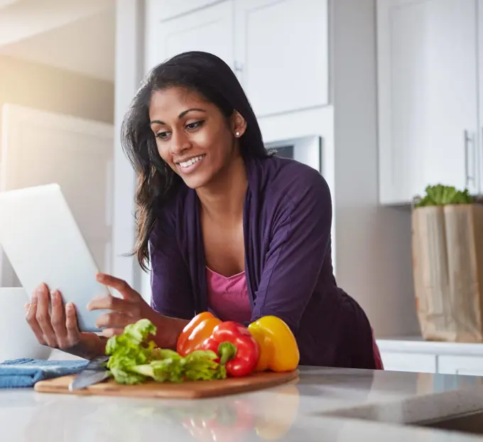 Loaded with recipes for a healthy lunch. a young woman using a digital tablet while preparing a healthy meal at home.