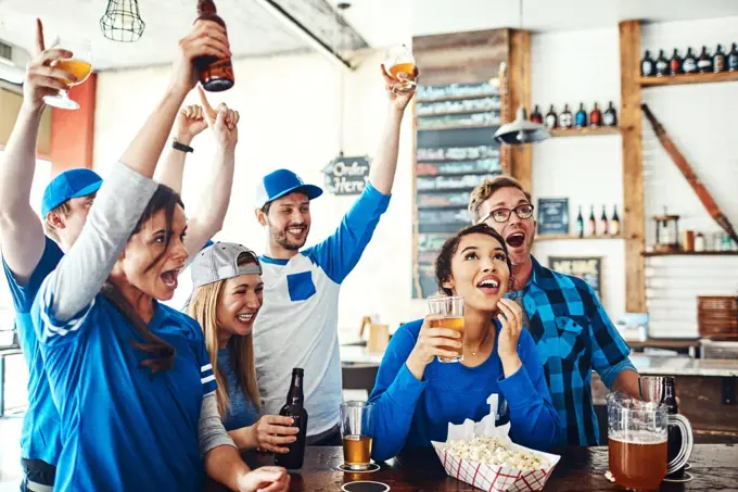 Die hard sports fans. a group of friends cheering while watching a sports game at a bar.