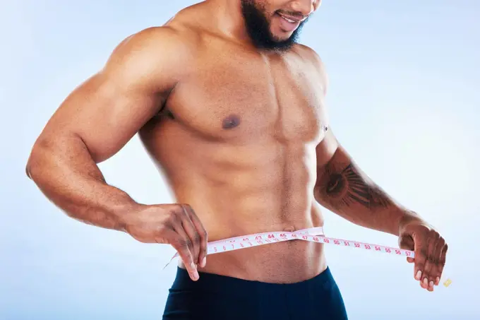 Black man, exercise and body, weightloss and measuring tape with health and active lifestyle on blue background. Shirtless male bodybuilder, abs and fitness with diet, healthy and strong in studio