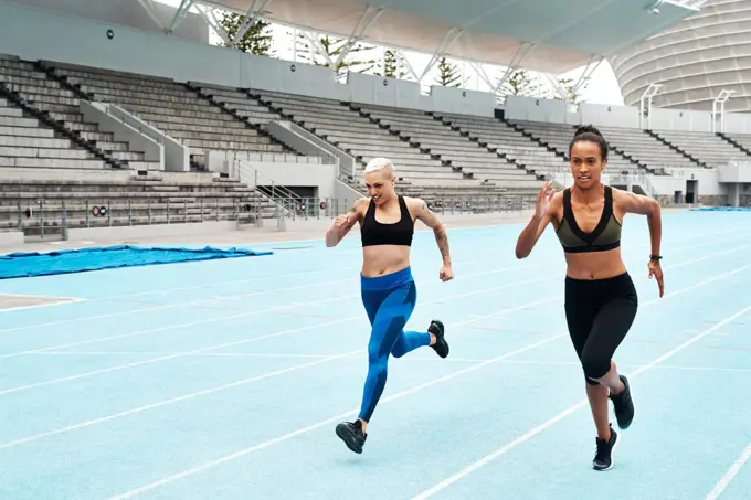 There is no finish line too far away. Full length shot of two attractive young athletes running a track field together during an outdoor workout session.