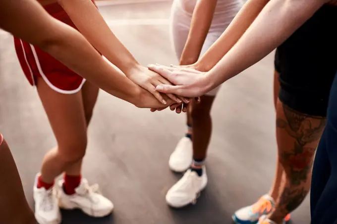 On three. an unrecognizable group of sportswomen piling their hands together before a basketball game.