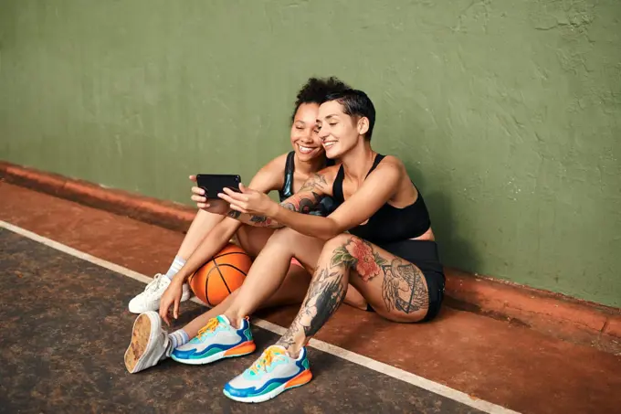 Lets get another selfie. two attractive sportswomen sitting together for a selfie after a basketball game during the day.