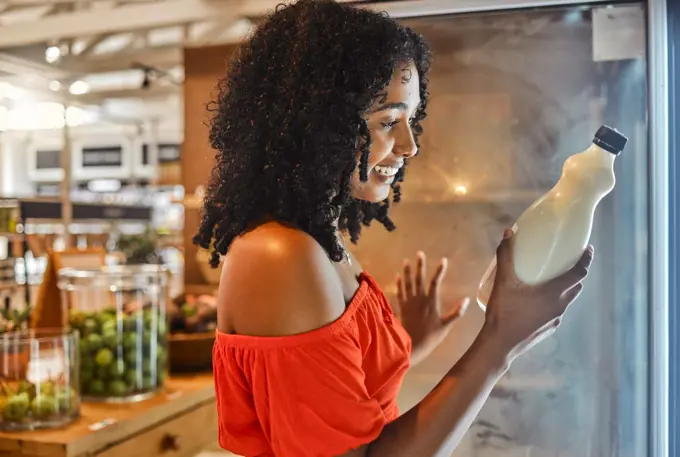 Woman, grocery shopping or reading milk label for sales date, vitamin information or calcium data in Brazilian store retail. Happy smile, supermarket customer or nutritionist and dairy fridge product