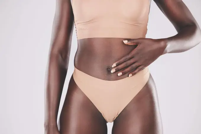 Hand, stomach and body with a model black woman touching her tummy in studio on a gray background for wellness. Health, underwear and diet with a female posing for healthy eating or lifestyle