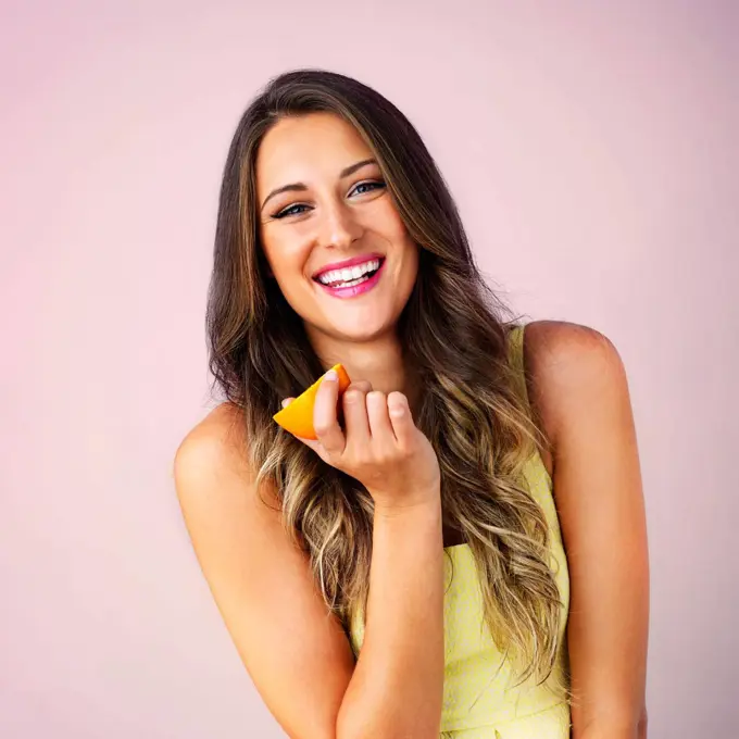 Eating healthy makes the mindset healthy. Studio shot of a young woman eating a orange against a pink background.