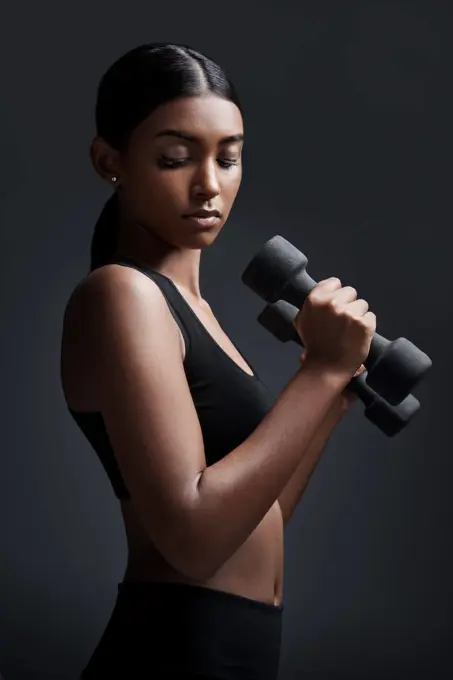 Sports, serious and woman with dumbbell for workout in studio isolated on a black background. Strong, bodybuilder and Indian female athlete weightlifting for muscle, training and fitness exercise.