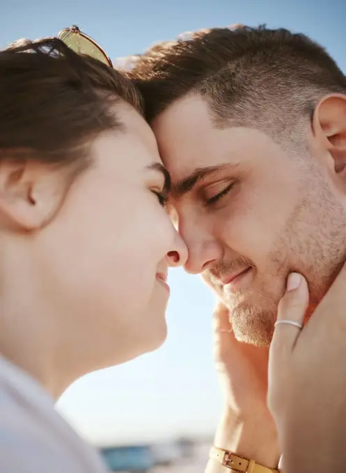 Love, touching face and couple on the beach, woman holding man with heads together. Summer, romance and loving happy couple on holiday. Real people, vacation and people in love bonding and affection