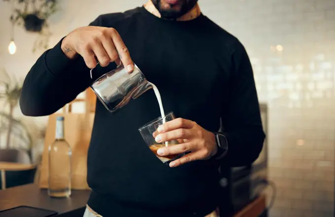 Coffee, milk and hands of man in cafe for cappuccino, breakfast and caffeine beverage. Relax, espresso and dairy with barista in coffee shop and with latte for retail, mocha and drink preparation