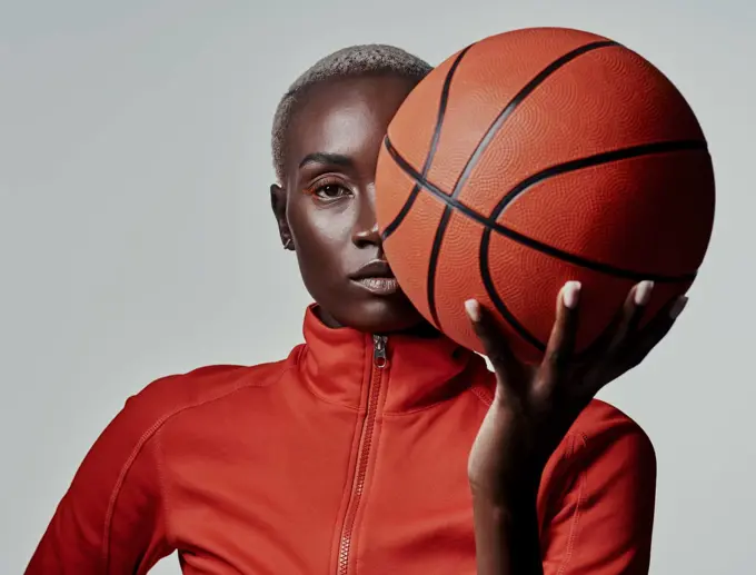 Call me the queen of the basketball court. Studio shot of an attractive young woman playing basketball against a grey background.