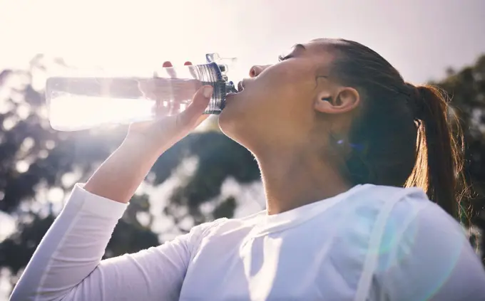 Drinking water, fitness and running with a sports woman outdoor for a cardio or endurance workout. Training, exercise and wellness with a female athlete taking a drink for hydration on a break