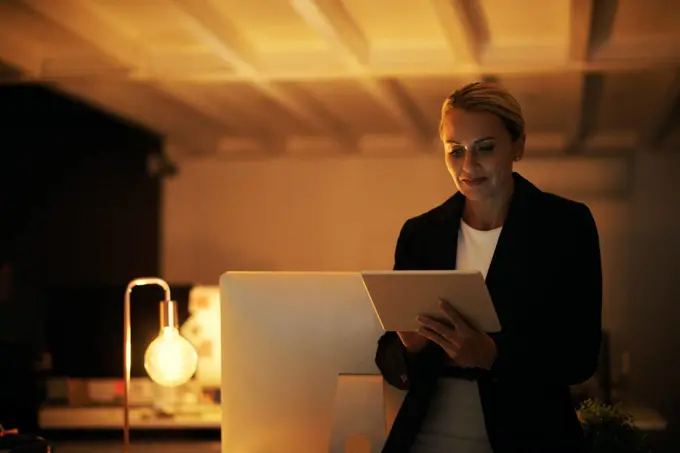 Working above and beyond office hours. a mature woman using her digital tablet while working late at the office.