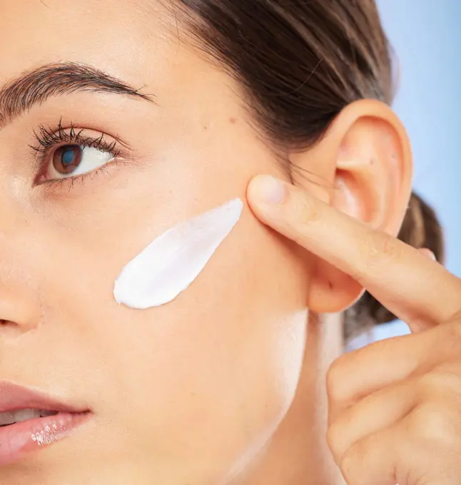 Face, beauty skincare and woman with cream in studio isolated on a blue background. Thinking, cosmetics and female model apply facial lotion, creme and moisturizer product for healthy skin hydration.