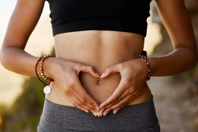 Woman, stomach and hand with heart in outdoor for exercise, diet, fitness and closeup. Female tummy, gut health and self love for wellness and training in the summer for healthy workout outside.