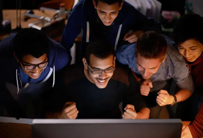 Getting behind the team. a group of young man cheering at a monitor in a dark room.