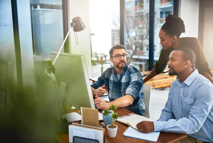 Coming together to achieve success. three businesspeople working around a computer in the office.