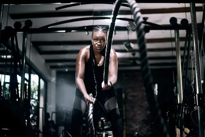 Ready for battle. Cropped portrait of an attractive young female athlete working out with battle ropes in the gym.