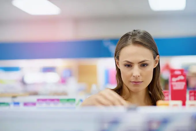 A young woman buying medicine in a pharmacy -The commercial designs displayed in this image represent a simulation of a real product and have been changed or altered enough by our team of retouching and design specialists so that they are free of any copyright infringements