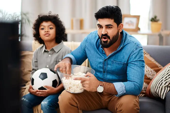 Were both avid sports fans. Cropped shot of an adorable little boy watching a football game with his father on tv at home.