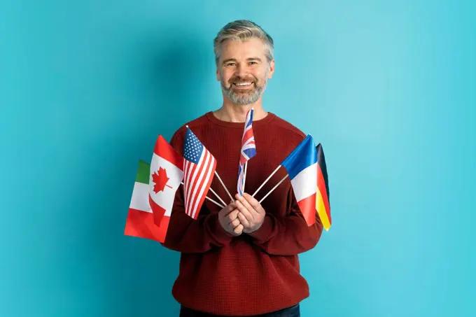 Cheerful grey-haired mature man holding flags of different countries