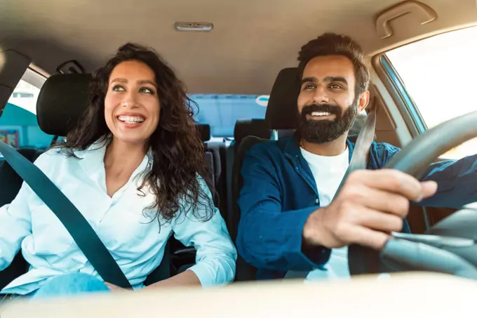 Joyful middle eastern spouses enjoying travel by car, sitting on front passengers seats in their new auto