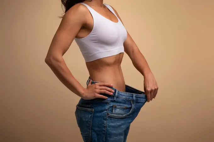 Cropped of lady in big jeans demonstrating results of diet