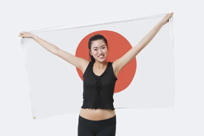 Portrait of smiling young woman holding Japanese flag over white background