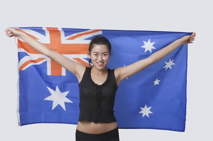 Portrait of smiling young woman holding Australian flag over white background