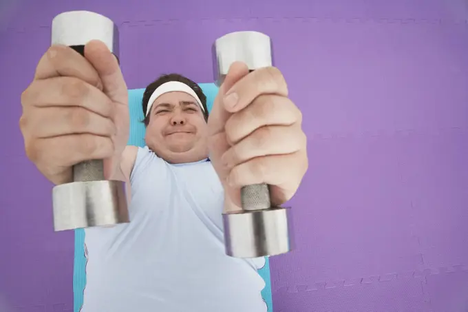 Overhead view of an overweight man lying down and lifting dumbbells