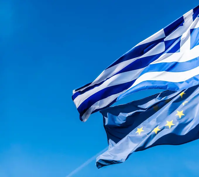 Flags of Greece and European Union on blue sky background, politics of Europe