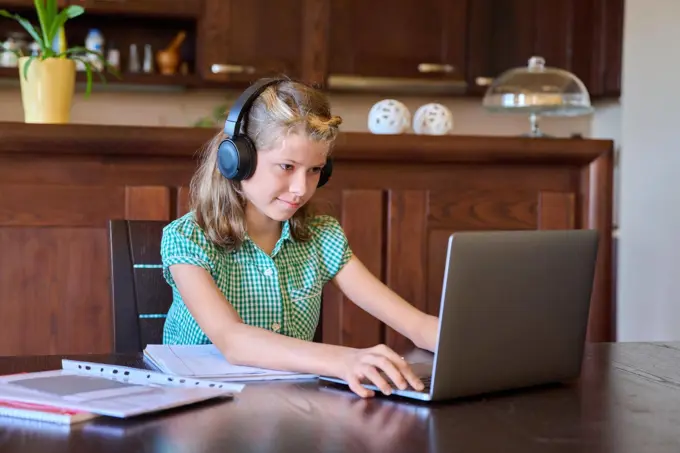 Pre-teen girl with laptop and headphones studies at home.