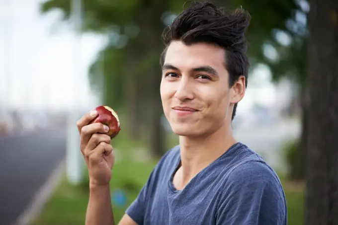 Man, smile and eating an apple, health and wellness in portrait, nutrition and vitamins for vegan. Happy male person, fruit and organic or natural, breakfast and diet in outdoors, fresh and digestion