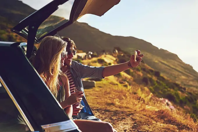 Roadtripping. a happy young couple posing for a selfie with their car on a roadtrip.