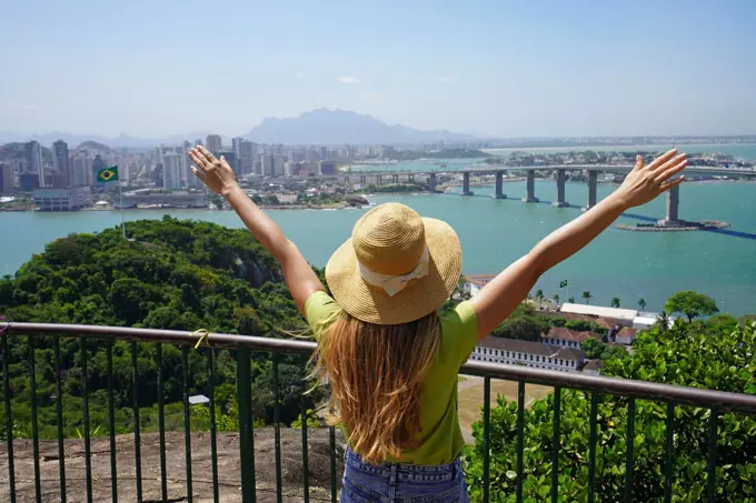 Joyful girl visiting Brazil. Beautiful young woman with raised arms enjoying view of Vitoria cityscape the capital of Espirito Santo state in Brazil.