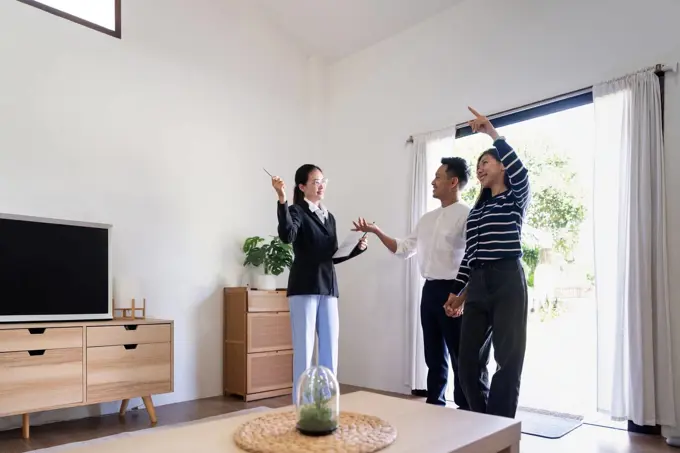 Young couple follow a real estate agent who is giving them a tour around a home, showing all the room and telling about all the advantage of living. Buying house or apartment concept