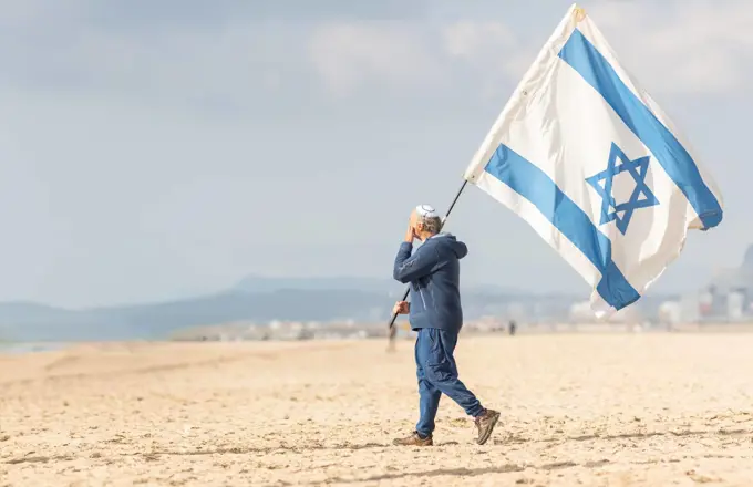 25 november 2023, Lisbon, Portugal - A Man Walking on a Beach Holding a Flag of Israel