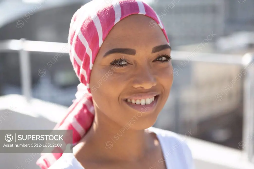 Portrait of smiling woman wearing scarf with breast cancer awareness against city background