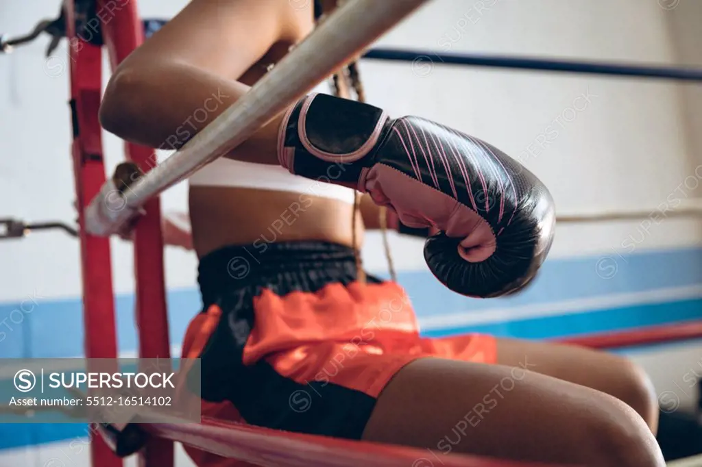 Close-up of female boxer relaxing in boxing ring at fitness center. Strong female fighter in boxing gym training hard.