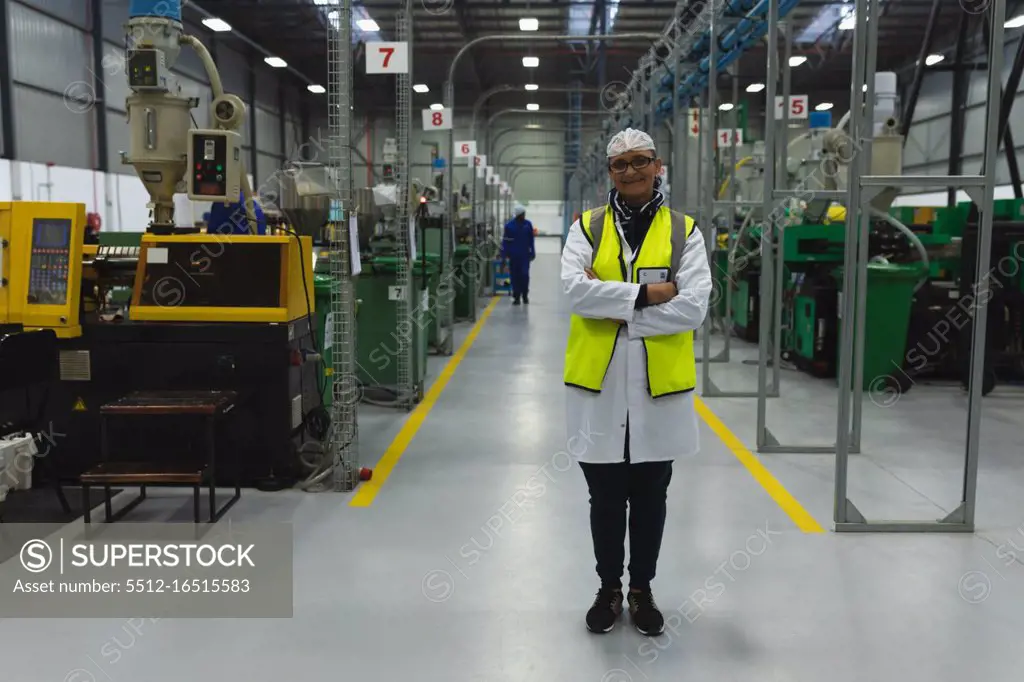 Portrait of a middle aged Caucasian woman wearing glasses and workwear standing between rows of equipment smiling in a warehouse at a processing plant, another worker visible in the background 