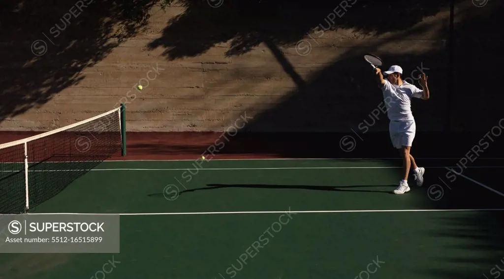 Side view of a young Caucasian man playing tennis on a sunny day, hitting a ball with a wall behind him